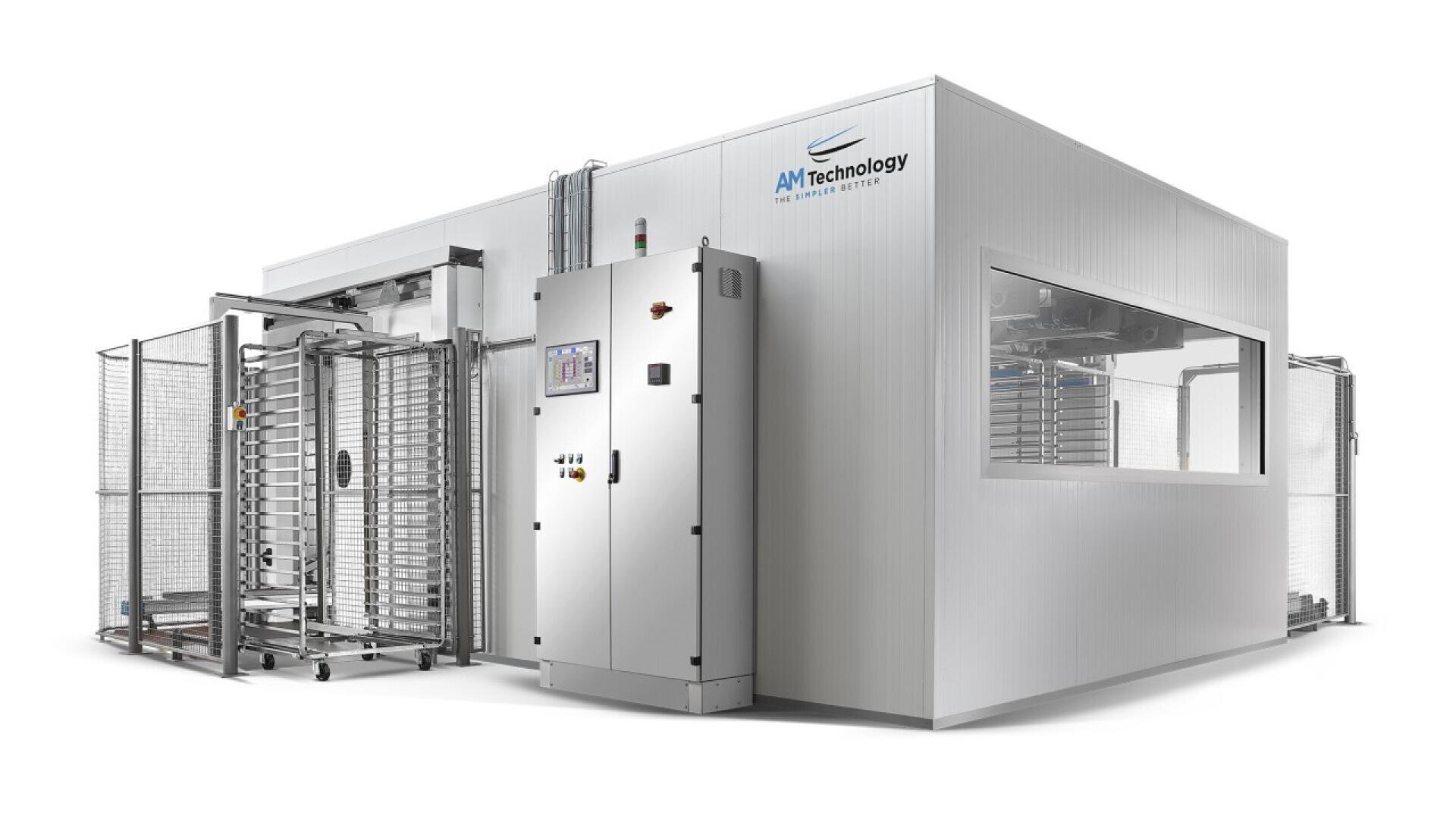 Eine große Industriemaschine von AM Technology mit Metallgestellen, Schalttafeln und transparenten Fenstern, die für die automatisierte Verarbeitung in einer sauberen, modernen Anlage ausgelegt ist.