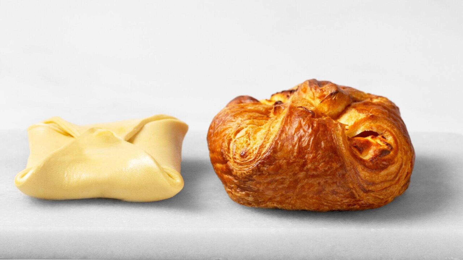 Two pastries are shown side by side on a white surface: one is unbaked and neatly folded, while the other is golden brown and fully baked, with a puffed and flaky appearance.