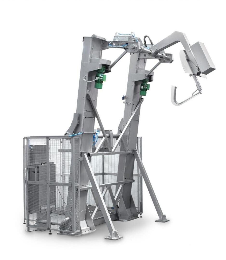 A large, industrial metal machine with vertical arms, green motor components, and a gated enclosure, designed for automated handling or processing tasks.