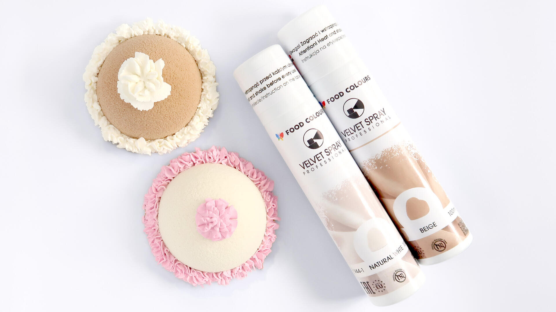 Two decorated round pastries, one with beige tones and white cream, the other with white and pink cream, next to two cans of Velvet Spray food color in beige and white on a white background.
