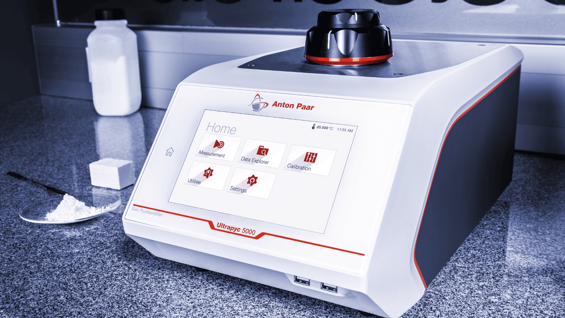 A laboratory instrument with a touchscreen display showing options like “Measurement,” “Data Explorer,” and “Calibration.” White powder, a spatula, and a jar are nearby on a gray countertop.