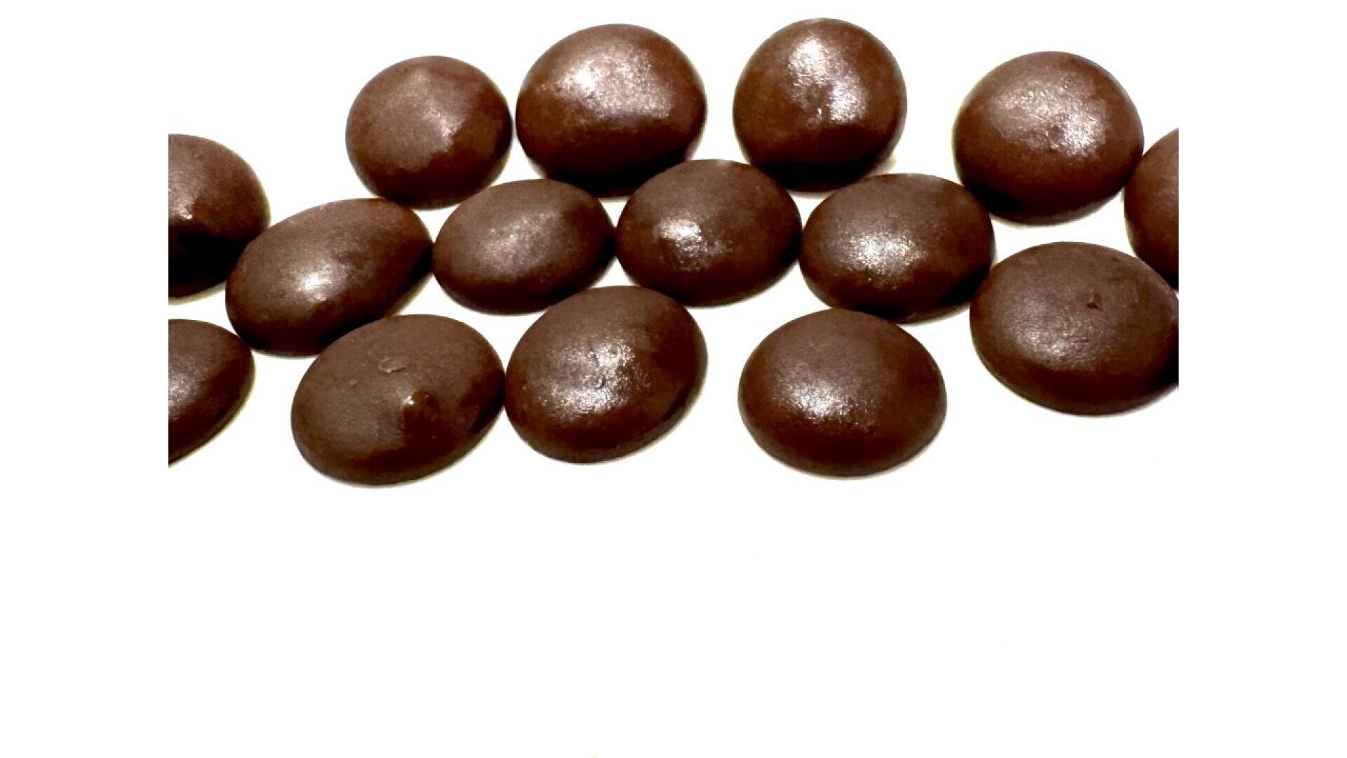 Runde, glänzende, dunkelbraune Schokoladenstücke, verstreut auf einer weißen Oberfläche.