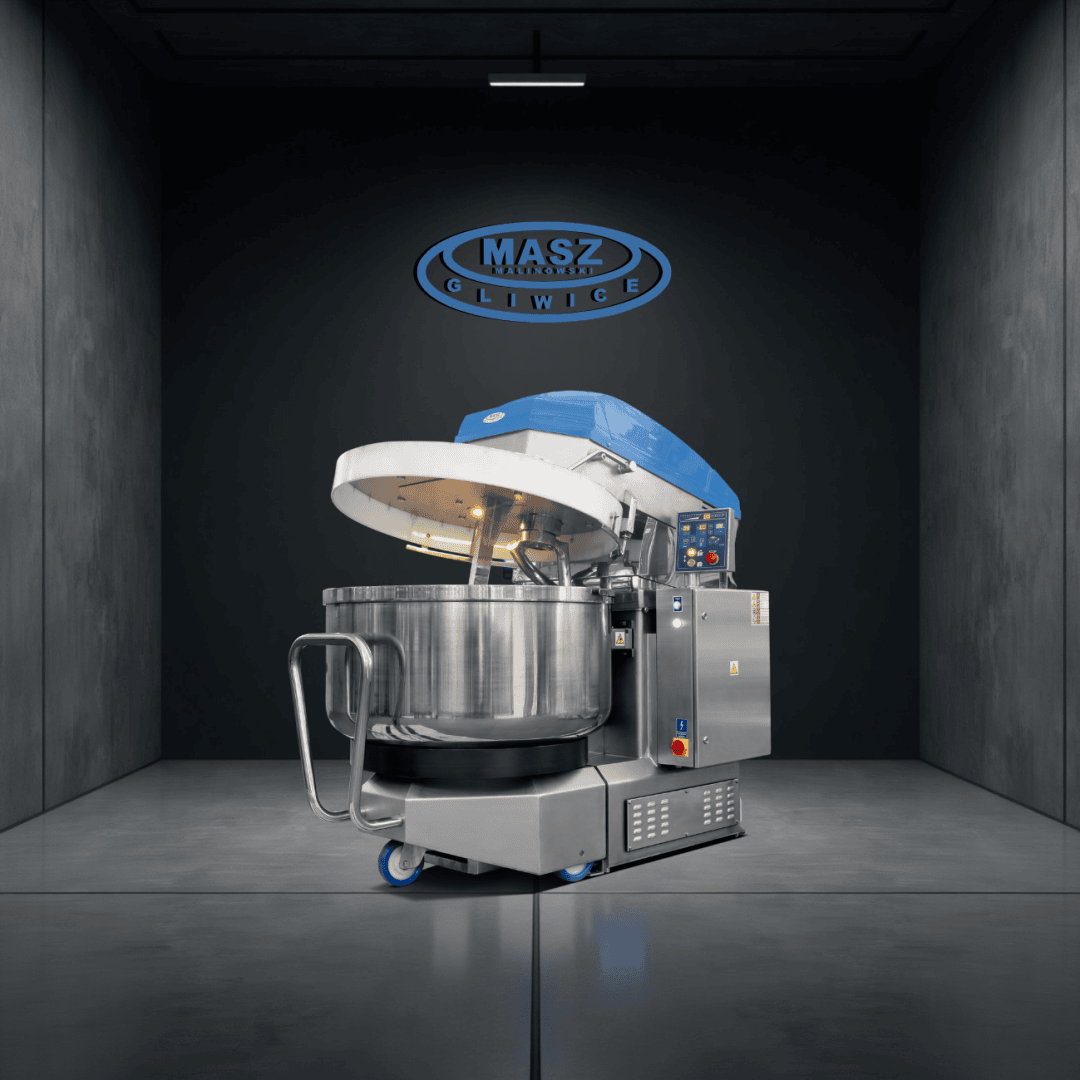 In einem modernen, dunklen Raum steht eine große industrielle Teigmaschine mit blauem Deckel und Edelstahlschüssel. An der Rückwand über der Maschine prangt das Logo von MASZ Gliwice.