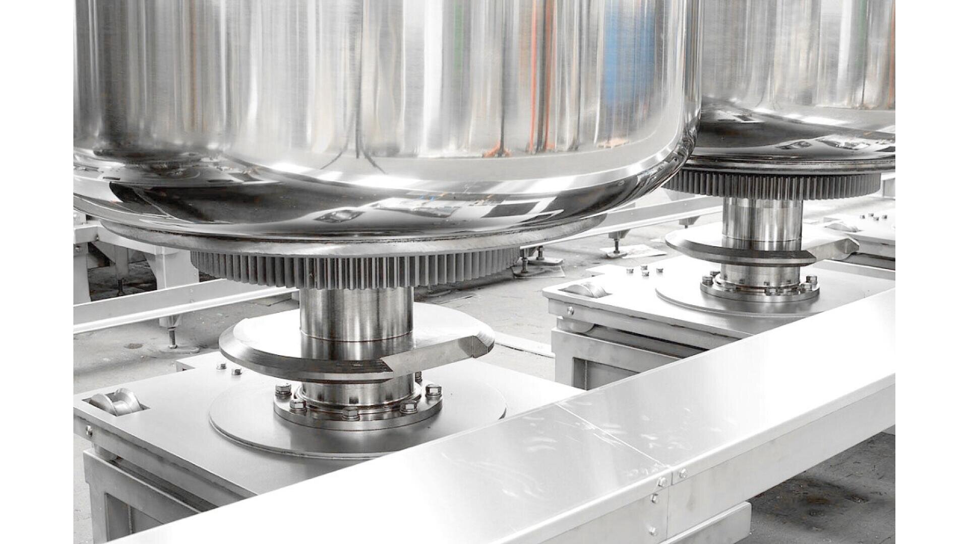 Nahaufnahme großer, glänzender Industrietanks aus Edelstahl mit polierten Oberflächen, die auf Metallfüßen stehen und auf mechanischen Plattformen in einer sauberen, modernen Anlage montiert sind.
