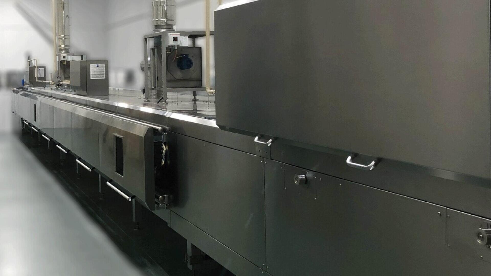 Eine große industrielle Lebensmittelverarbeitungsmaschine aus rostfreiem Stahl mit mehreren Fächern und Bedienfeldern in einer sauberen, modernen Fabrikumgebung.