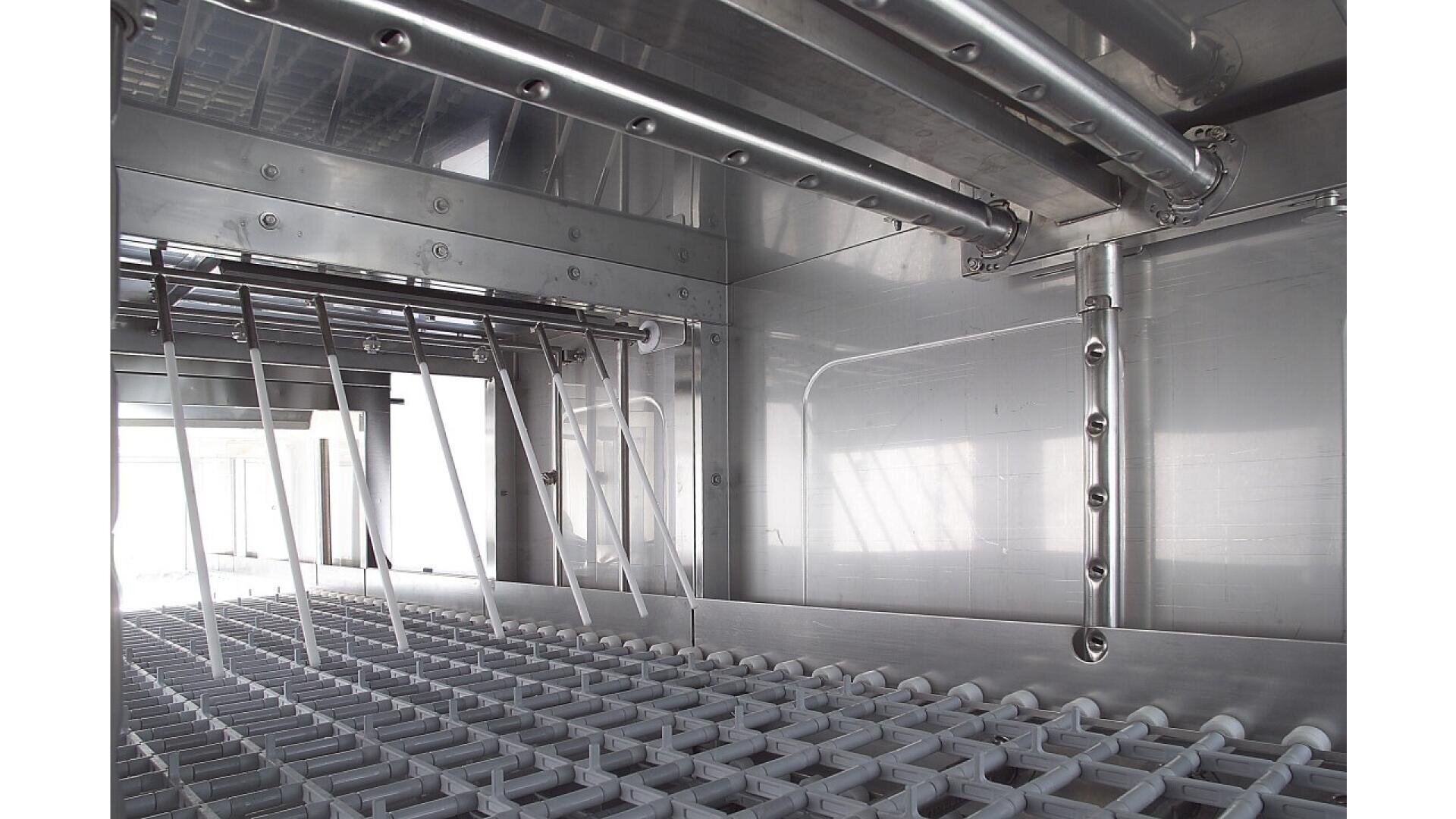 Innenansicht einer industriellen Geschirrspülmaschine mit Metallgestellen, Sprühdüsen und Edelstahlwänden, die für die Reinigung großer Mengen von Küchengeräten konzipiert ist.