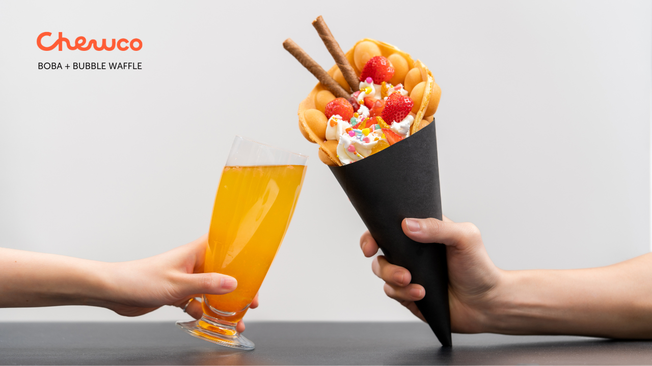 A hand holds a glass of orange drink clinking with another hand holding a black cone filled with bubble waffle, whipped cream, strawberries, sprinkles, and wafer sticks. Chewco BOBA + BUBBLE WAFFLE is in the top left corner.