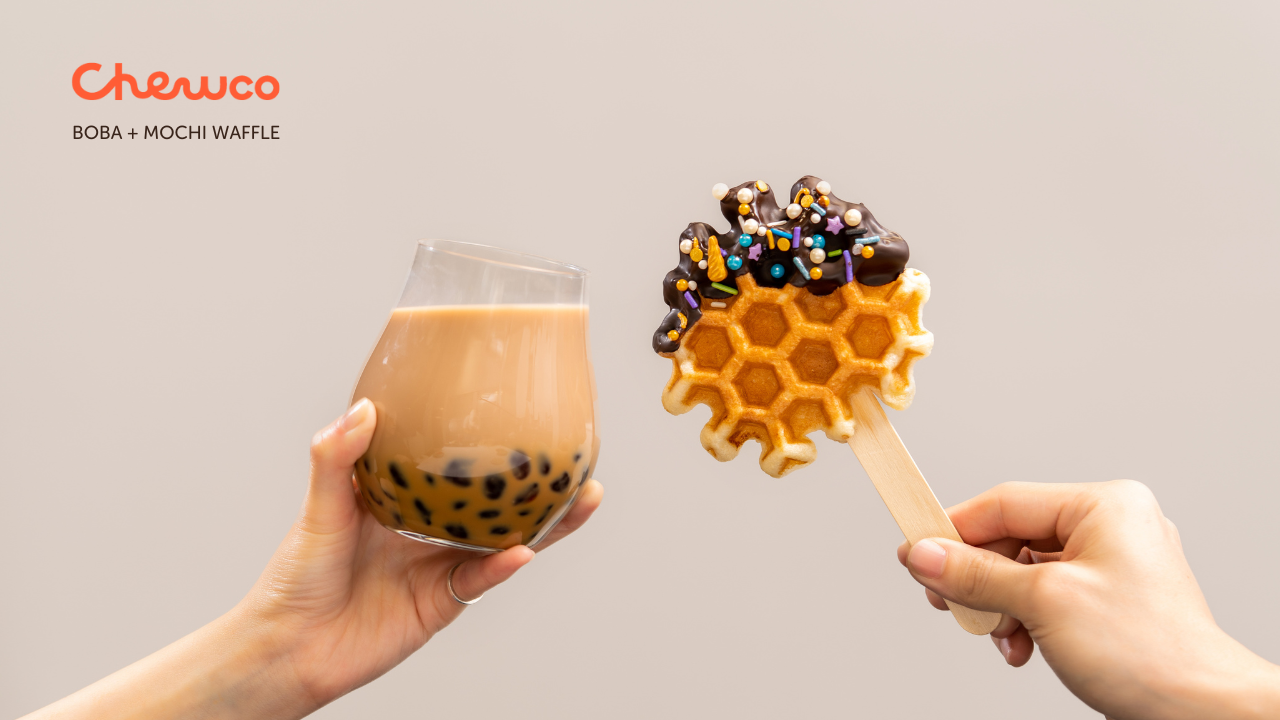 One hand holds a glass of bubble tea with brown tapioca pearls, while another hand holds a honeycomb-shaped mochi wafer on a stick, covered in chocolate and colorful sprinkles. The Chewco logo appears in the corner.