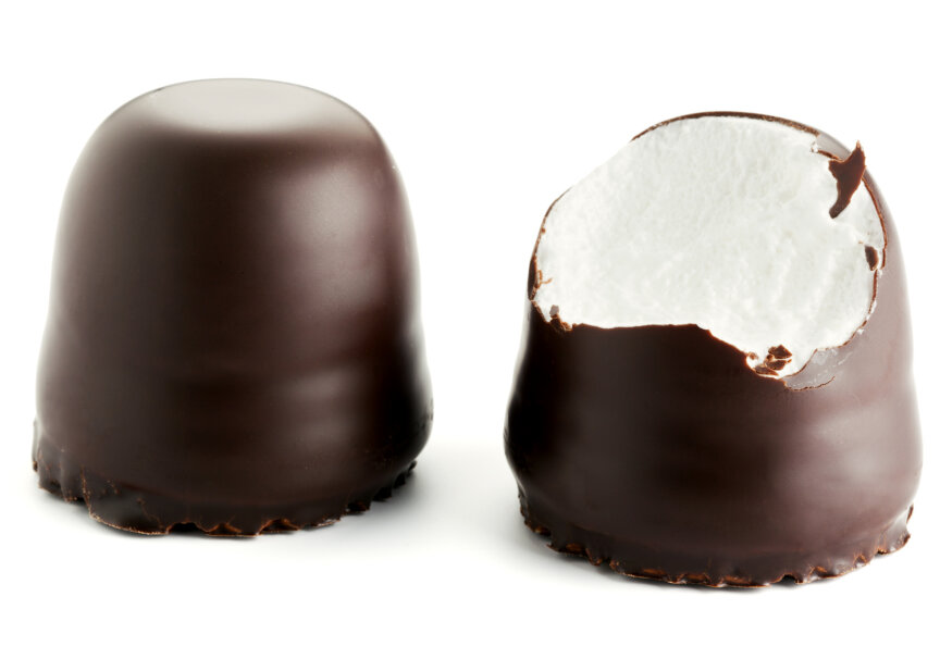 Two chocolate-covered marshmallow treats are shown; one is whole, and the other is bitten to reveal the fluffy white filling inside, both set against a white background.